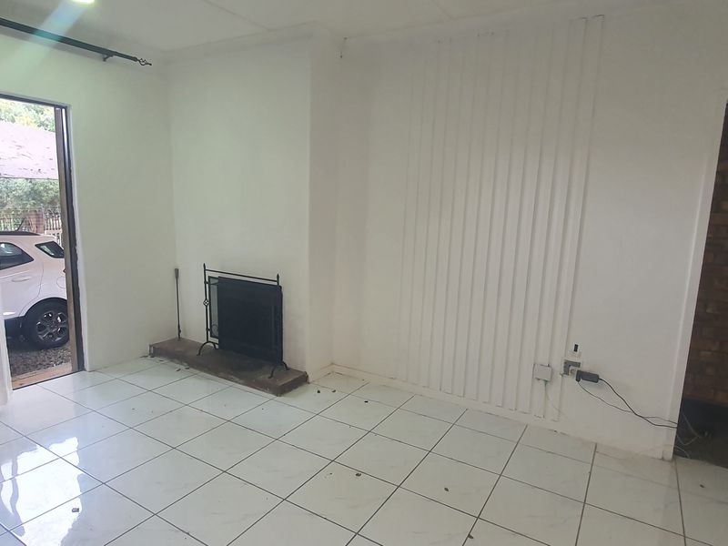 An empty living room featuring tiled flooring, a built-in fireplace, and an exposed brick wall section, offering a blank canvas for renovation.
