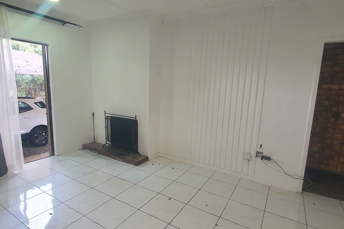 An empty living room featuring tiled flooring, a built-in fireplace, and an exposed brick wall section, offering a blank canvas for renovation.