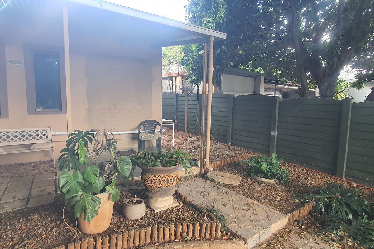 A rear exterior view featuring a covered patio area, paved pathways, and a private garden enclosed by a precast concrete boundary wall.