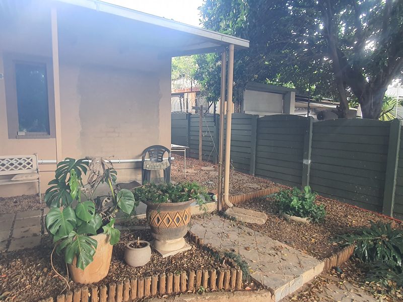 A rear exterior view featuring a covered patio area, paved pathways, and a private garden enclosed by a precast concrete boundary wall.