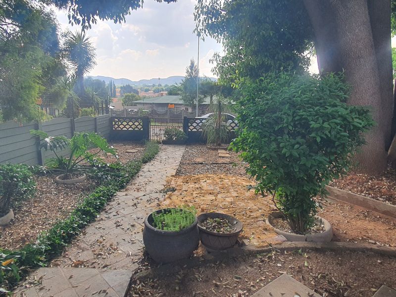 A private garden area featuring a paved pathway, mature trees, and boundary fencing, offering a view towards the surrounding neighborhood.