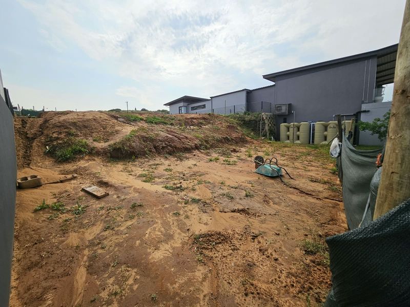 A view of the rear yard area featuring uneven terrain, exposed soil, and installed water storage tanks adjacent to the main building structure.