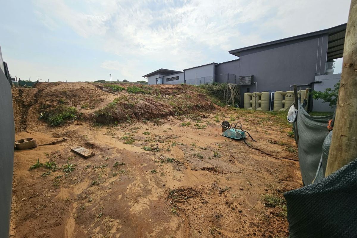 A view of the rear yard area featuring uneven terrain, exposed soil, and installed water storage tanks adjacent to the main building structure.