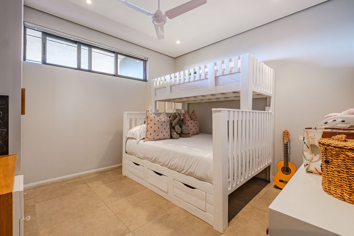 A well-maintained bedroom featuring neutral tiled flooring, recessed downlighting, a ceiling fan, and a high-set horizontal window for natural light.