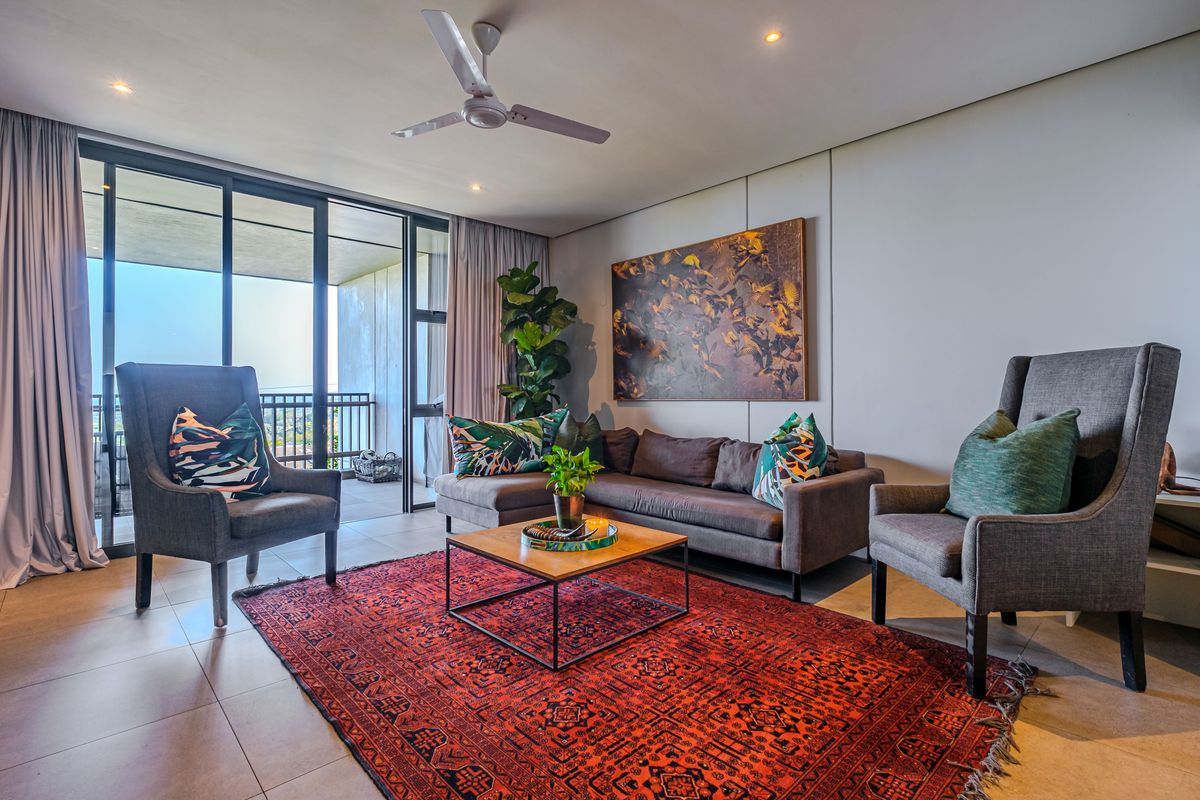 A well-lit living room featuring large sliding glass doors leading to a balcony, neutral tiled flooring, and a modern ceiling fan.