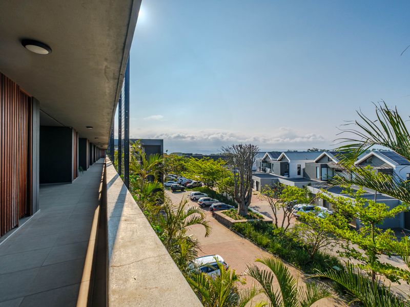 A spacious covered balcony featuring modern tiled flooring, timber slat accents, and recessed lighting, offering an elevated view of the surrounding residential complex.