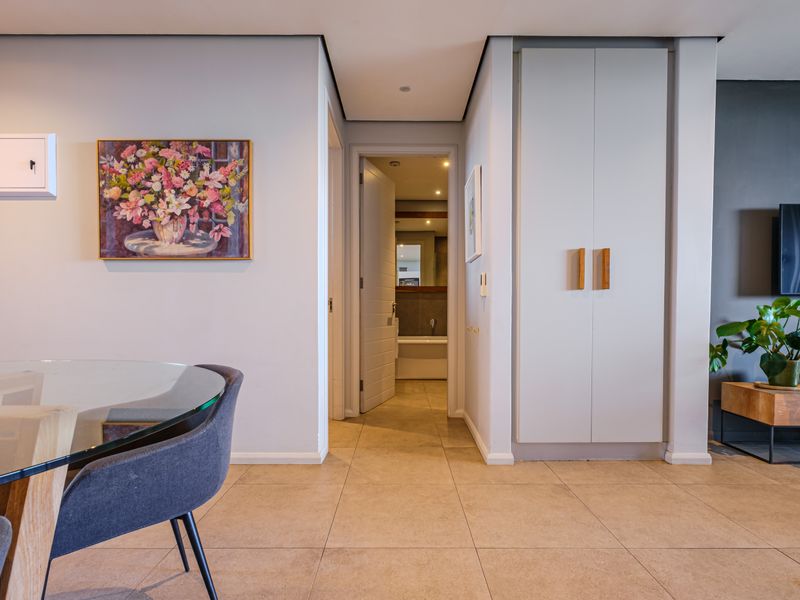 A well-maintained hallway featuring neutral tiled flooring, recessed ceiling lighting, and a built-in storage cupboard, providing access to adjacent rooms.