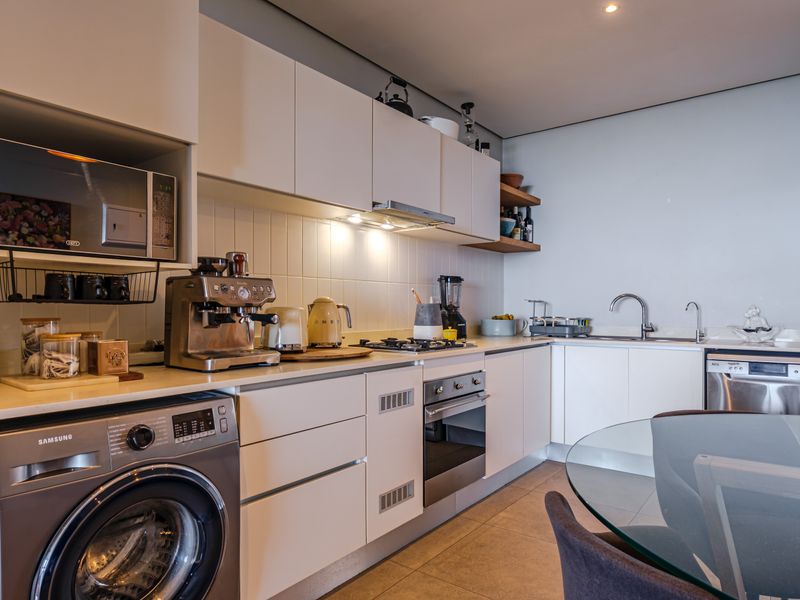 Modern kitchen featuring sleek white cabinetry, stone countertops, integrated appliances, gas hob, and a tiled backsplash in a clean, functional layout.
