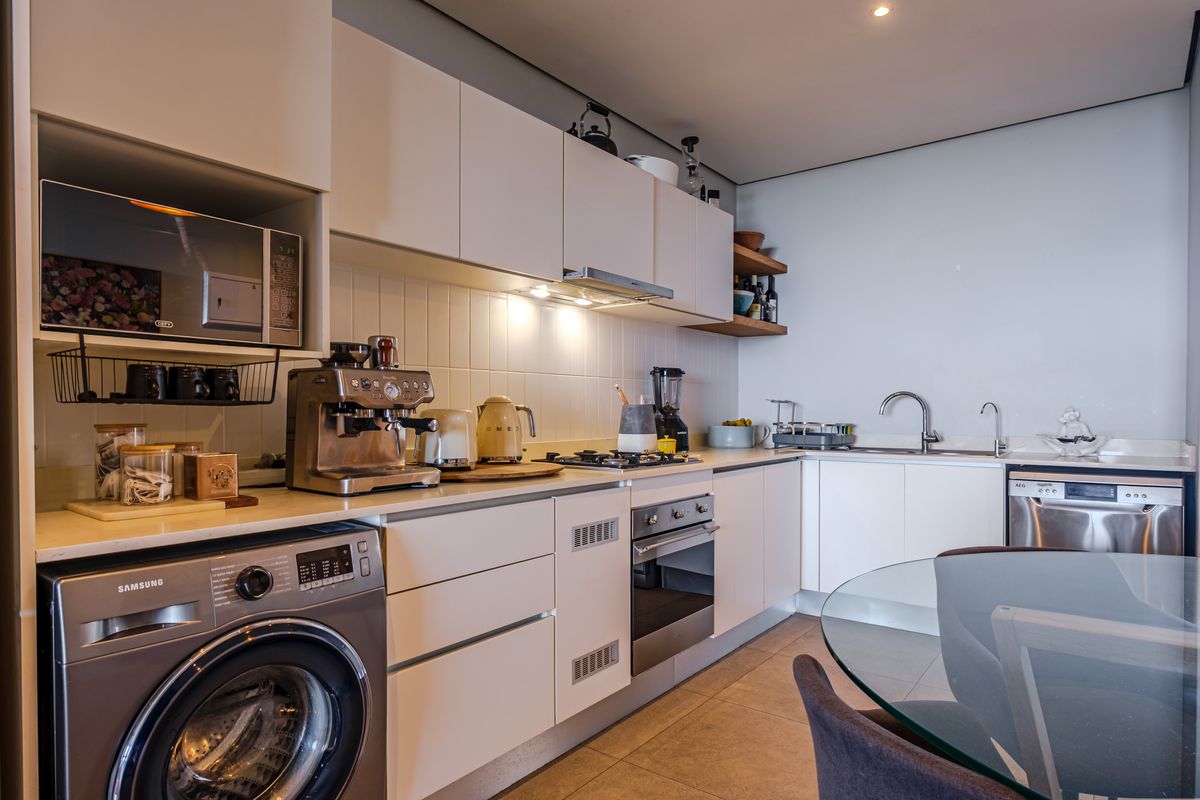Modern kitchen featuring sleek white cabinetry, stone countertops, integrated appliances, gas hob, and a tiled backsplash in a clean, functional layout.