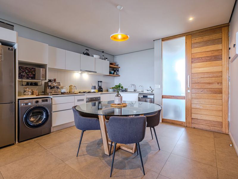 Modern open-plan kitchen and dining area featuring sleek cabinetry, tiled floors, integrated appliances, and a distinctive timber sliding door.