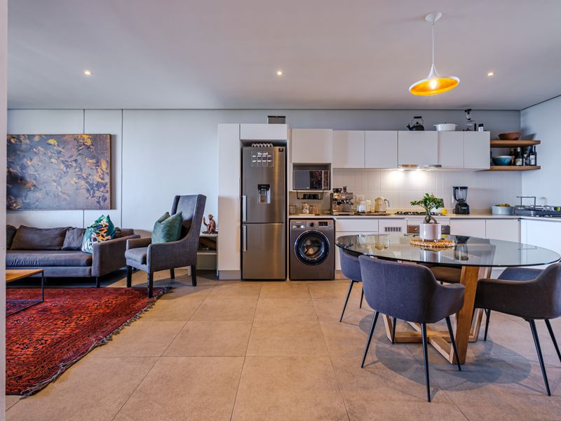 Modern open-plan living area featuring a sleek kitchen with integrated appliances, tiled flooring, and recessed lighting, seamlessly flowing into the lounge space.