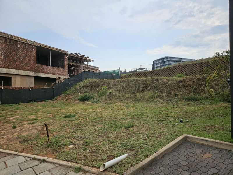 A view of a vacant residential plot featuring a retaining wall and an adjacent building currently under construction.