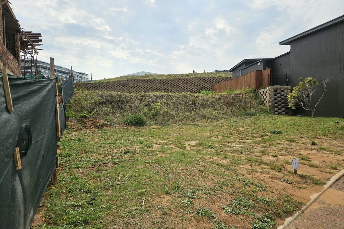 A vacant residential plot featuring a tiered retaining wall, timber fencing, and a paved driveway area, ready for development.