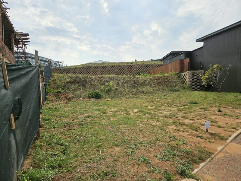 A vacant residential plot featuring a tiered retaining wall, timber fencing, and a paved driveway area, ready for development.