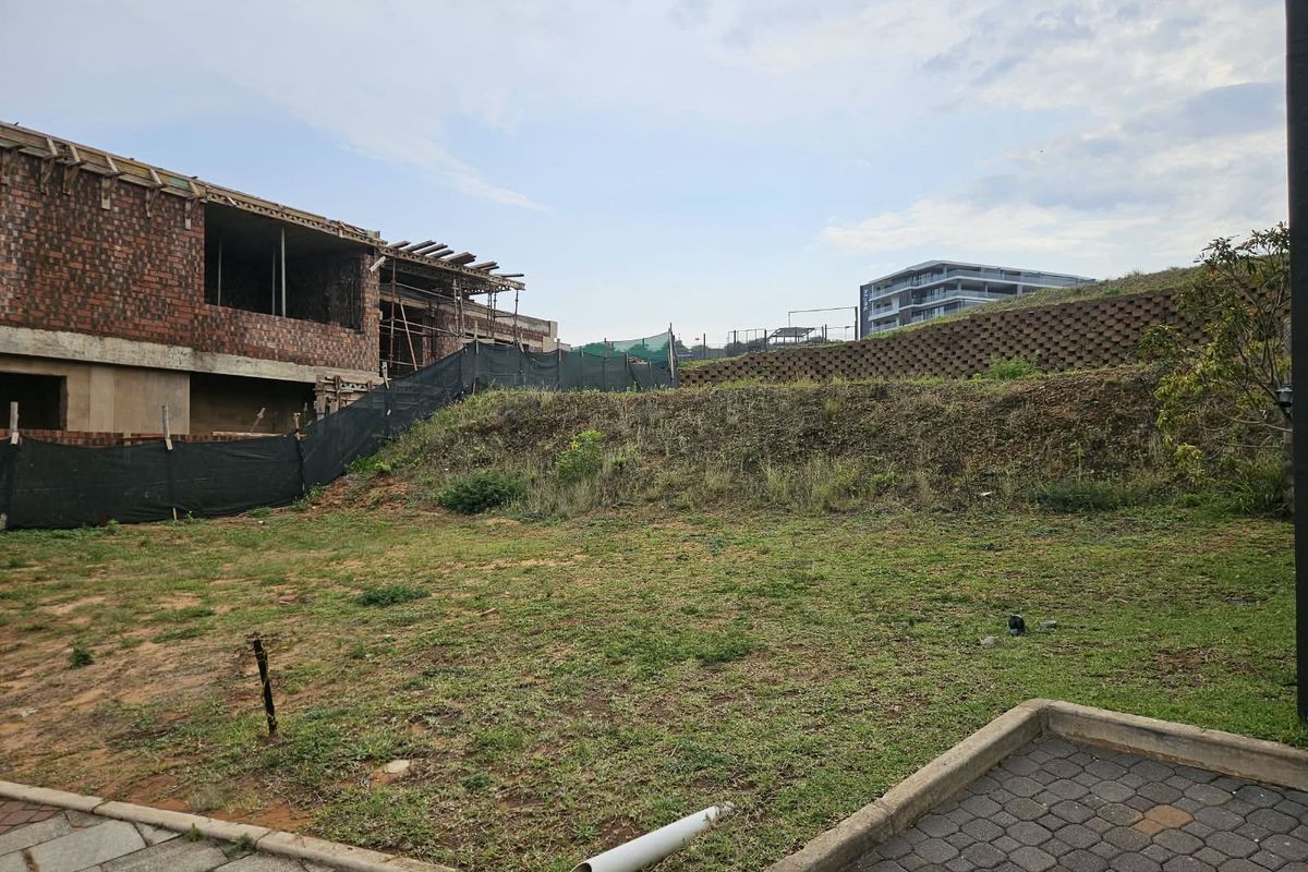 A view of a vacant residential plot featuring a retaining wall and an adjacent building currently under construction.
