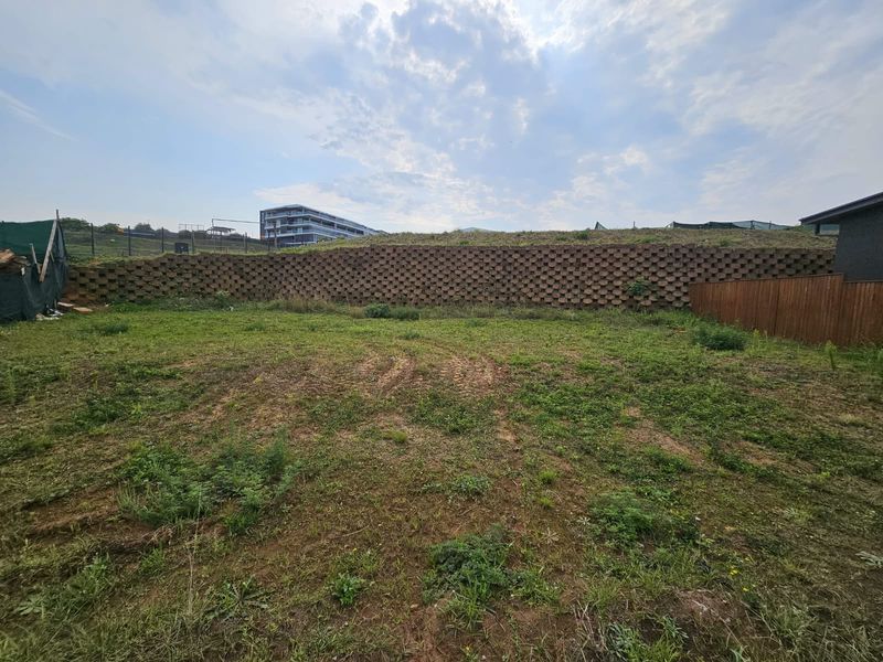 A vacant residential plot featuring a large concrete block retaining wall and perimeter timber fencing, ready for development.
