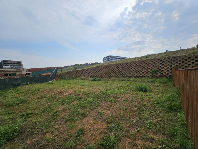 A vacant residential plot featuring a tiered concrete retaining wall and timber boundary fencing, ready for development.