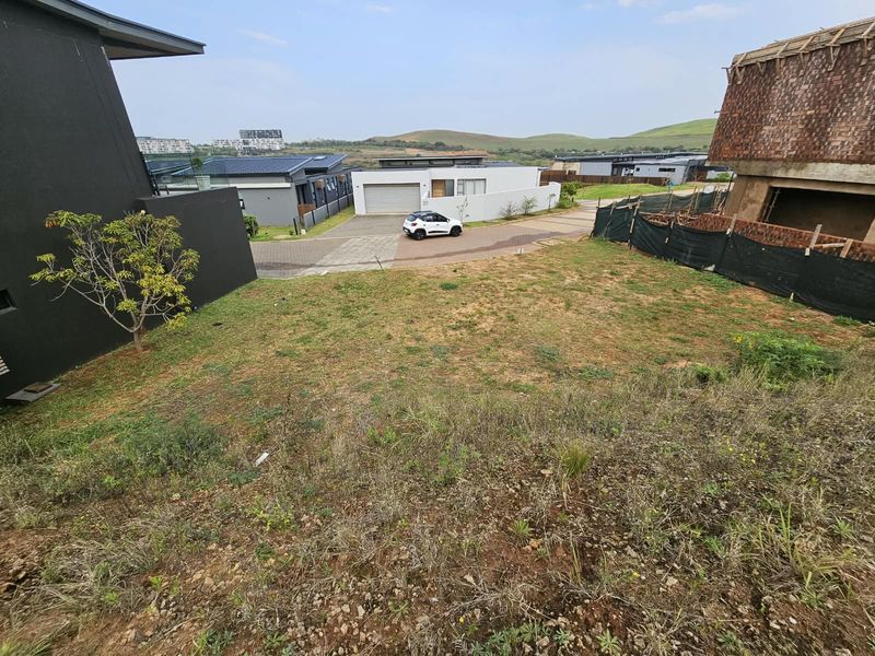 A vacant residential plot of land with a gentle slope, situated in a developed estate with surrounding modern homes.