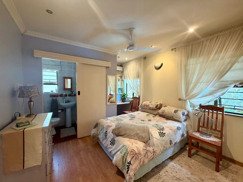 A bedroom featuring laminate flooring, a ceiling fan, and an en-suite bathroom with a pedestal sink, accessed via a sliding door.