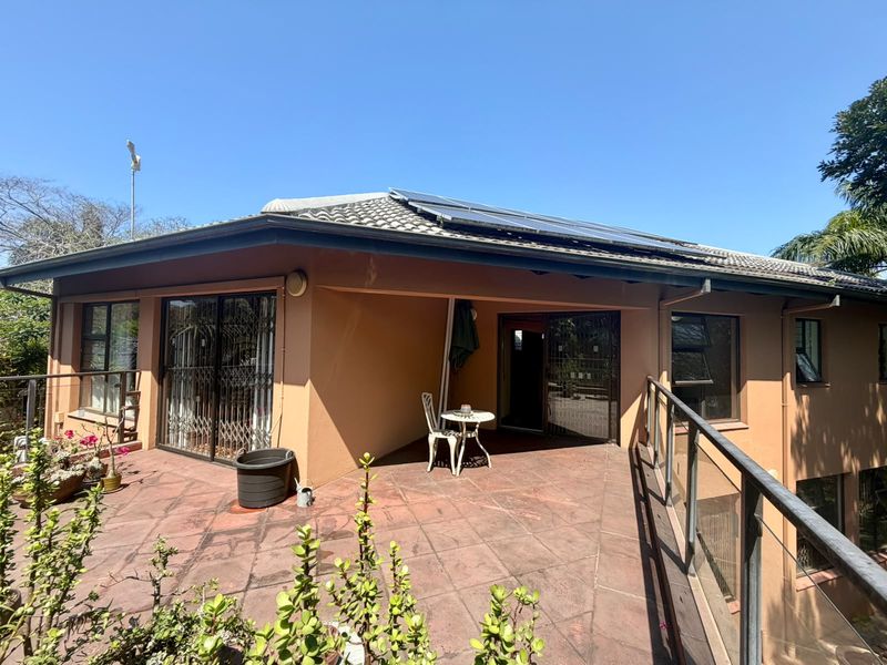 A spacious elevated patio area featuring tiled flooring, glass balustrades, and direct access to the home through sliding doors, topped with roof-mounted solar panels.