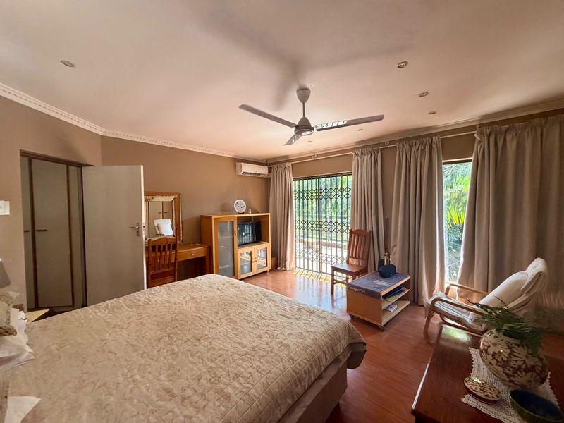 Spacious bedroom featuring laminate flooring, built-in wardrobes, a ceiling fan, and direct access to the exterior through a security gate.