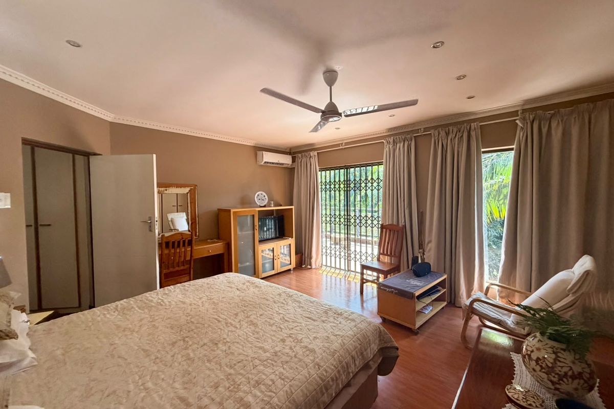 Spacious bedroom featuring laminate flooring, built-in wardrobes, a ceiling fan, and direct access to the exterior through a security gate.