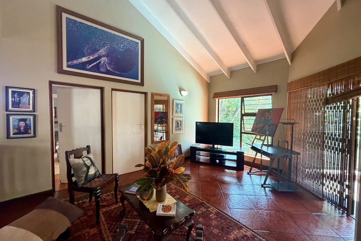 Spacious living room featuring a high vaulted ceiling with exposed beams, terracotta tiled flooring, and large windows providing natural light.