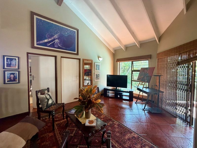 Spacious living room featuring a high vaulted ceiling with exposed beams, terracotta tiled flooring, and large windows providing natural light.