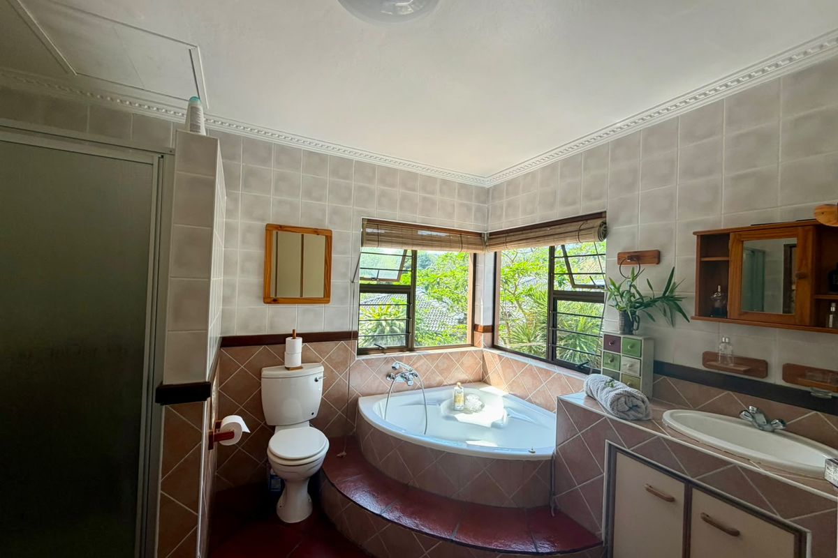 A dated bathroom featuring a corner bathtub, built-in vanity, shower enclosure, and tiled finishes with large windows providing natural light.