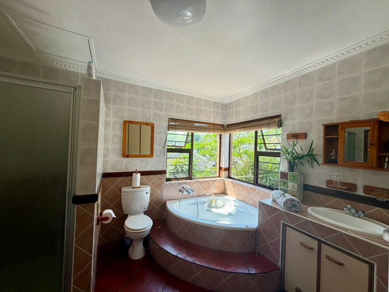 A dated bathroom featuring a corner bathtub, built-in vanity, shower enclosure, and tiled finishes with large windows providing natural light.