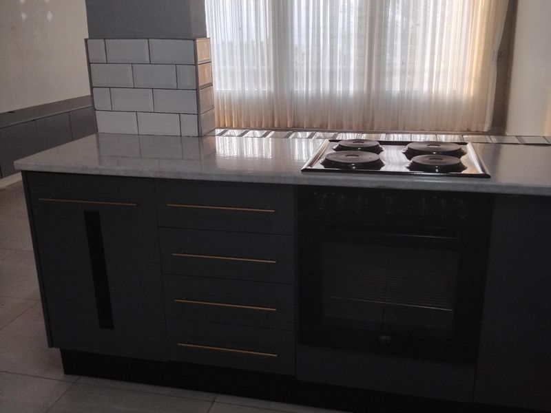 Modern kitchen featuring a central island with built-in oven, electric hob, and stylish subway tile detailing, set against a bright, airy window backdrop.