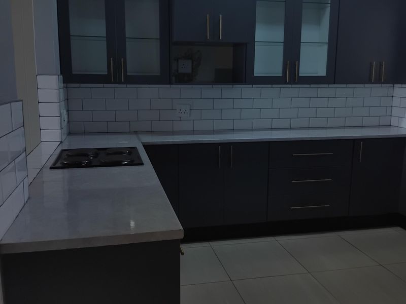 Modern kitchen featuring dark cabinetry, white subway tile backsplash, stone countertops, and a built-in electric hob with tiled flooring.