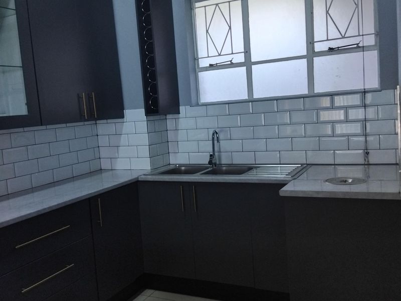 Modern kitchen featuring dark grey cabinetry, white subway tile backsplash, stone countertops, and a stainless steel double sink with natural light.