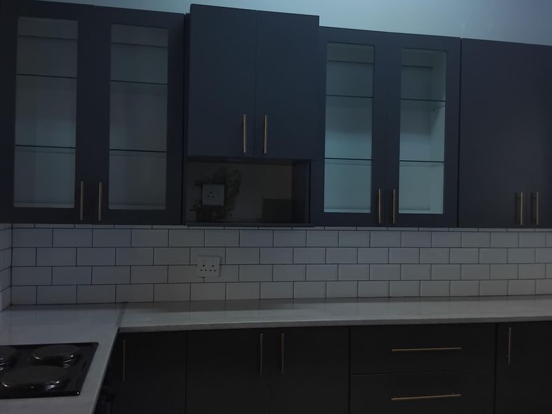 Modern kitchen featuring dark cabinetry, subway tile backsplash, stone countertops, integrated electric hob, and exposed timber ceiling beams.
