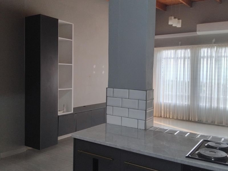 Modern open-plan living and kitchen area featuring dark cabinetry, stone countertops, subway tile accents, and exposed timber ceiling beams with a bright, airy feel.