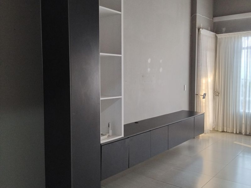 A spacious living area featuring modern built-in cabinetry, large format floor tiles, and an exposed timber ceiling, offering a clean canvas for interior design.