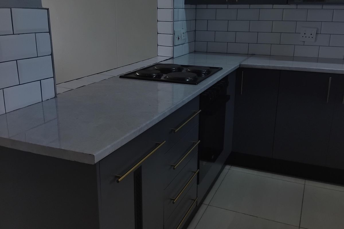Modern kitchen featuring dark grey cabinetry, stone countertops, subway tile backsplash, and integrated appliances in a clean, contemporary layout.