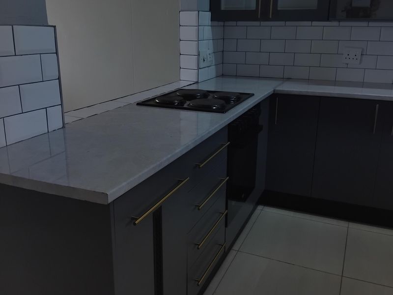 Modern kitchen featuring dark grey cabinetry, stone countertops, subway tile backsplash, and integrated appliances in a clean, contemporary layout.