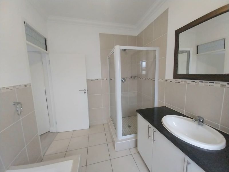 A clean, functional bathroom featuring a glass shower enclosure, a vanity with a granite countertop, and neutral wall and floor tiling.