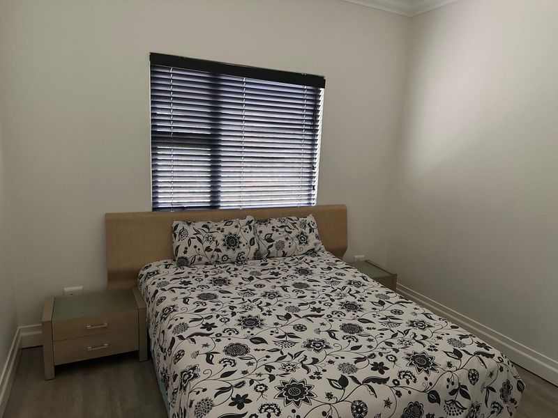 A clean and well-maintained bedroom featuring neutral walls, modern grey flooring, and fitted venetian blinds.