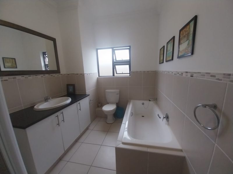 A clean, functional bathroom featuring a vanity with basin, a standard bathtub, and a toilet, finished with neutral wall and floor tiling.