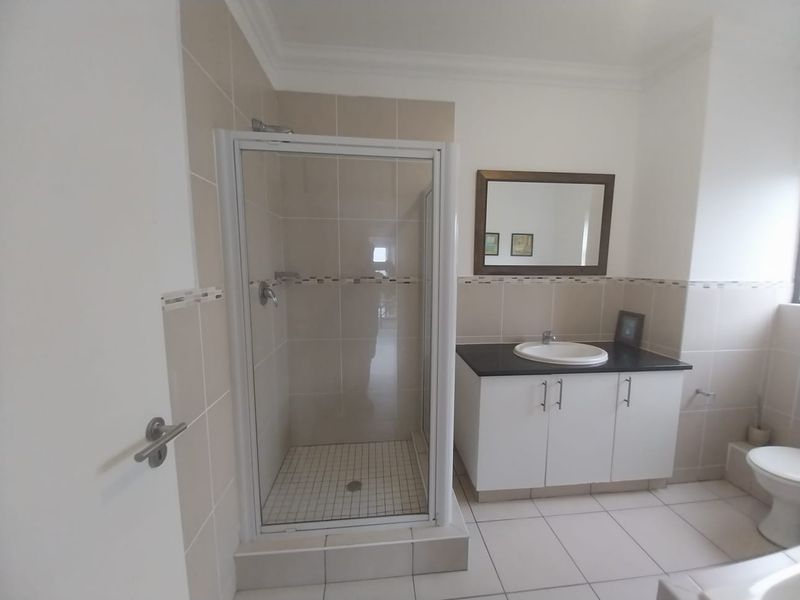 A clean, functional bathroom featuring a glass shower enclosure, a vanity with a basin, and neutral wall and floor tiling.