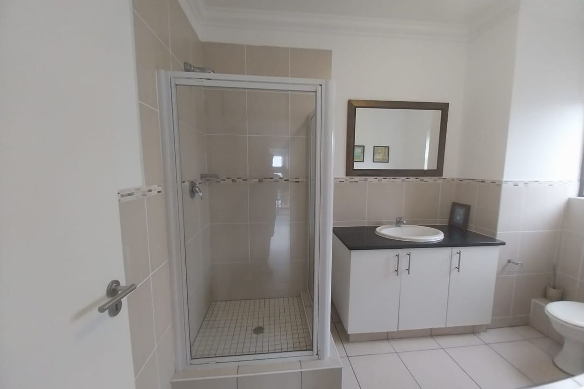 A clean, functional bathroom featuring a glass shower enclosure, a vanity with a basin, and neutral wall and floor tiling.