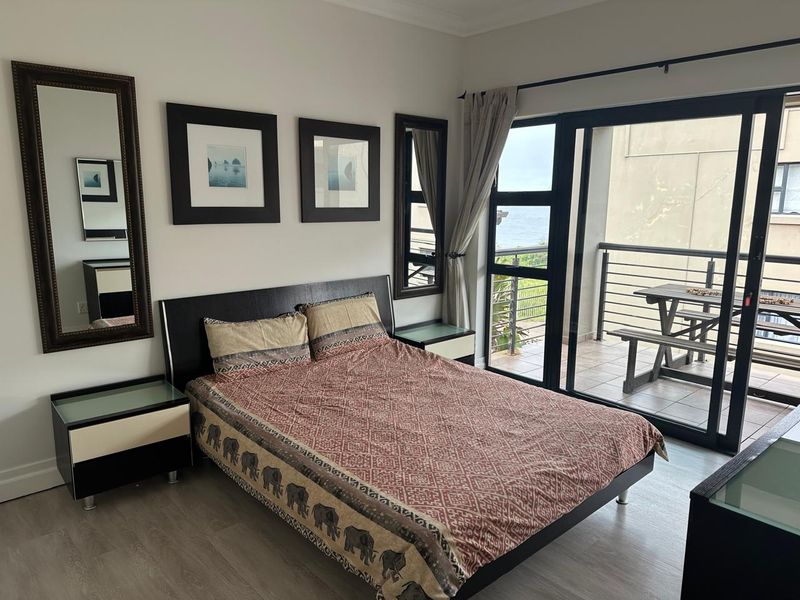 A well-maintained bedroom featuring modern laminate flooring and large sliding glass doors that provide direct access to a private balcony with ocean views.