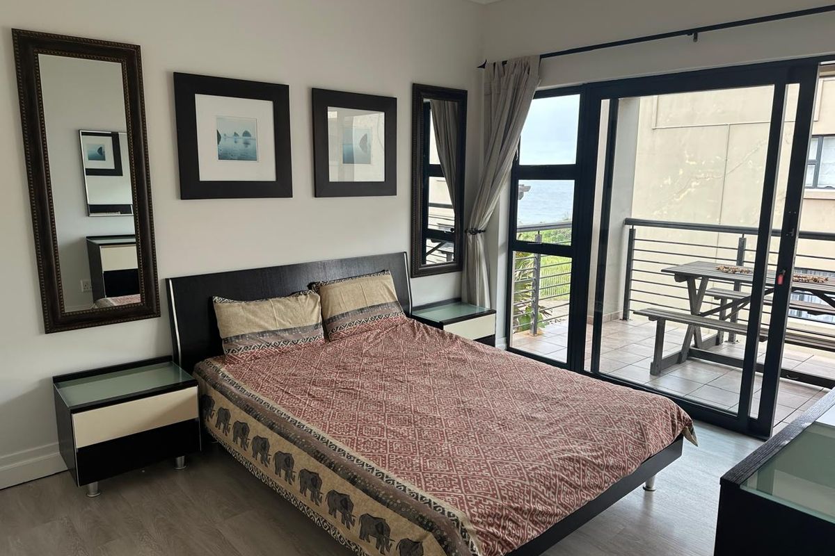 A well-maintained bedroom featuring modern laminate flooring and large sliding glass doors that provide direct access to a private balcony with ocean views.