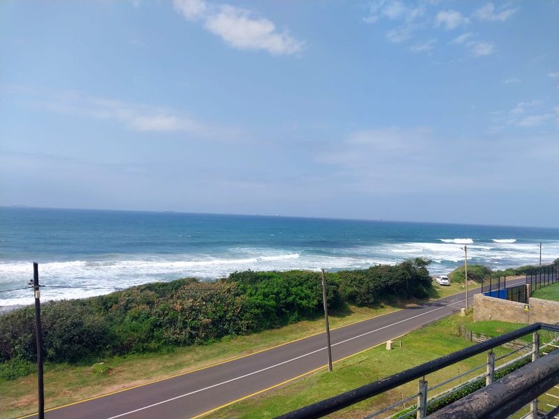 A scenic elevated view overlooking the coastal road, lush greenery, and the ocean horizon.