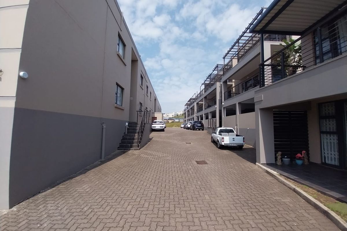 A view of the paved driveway and rear facade of the townhouse complex, featuring multi-level balconies and external staircases.