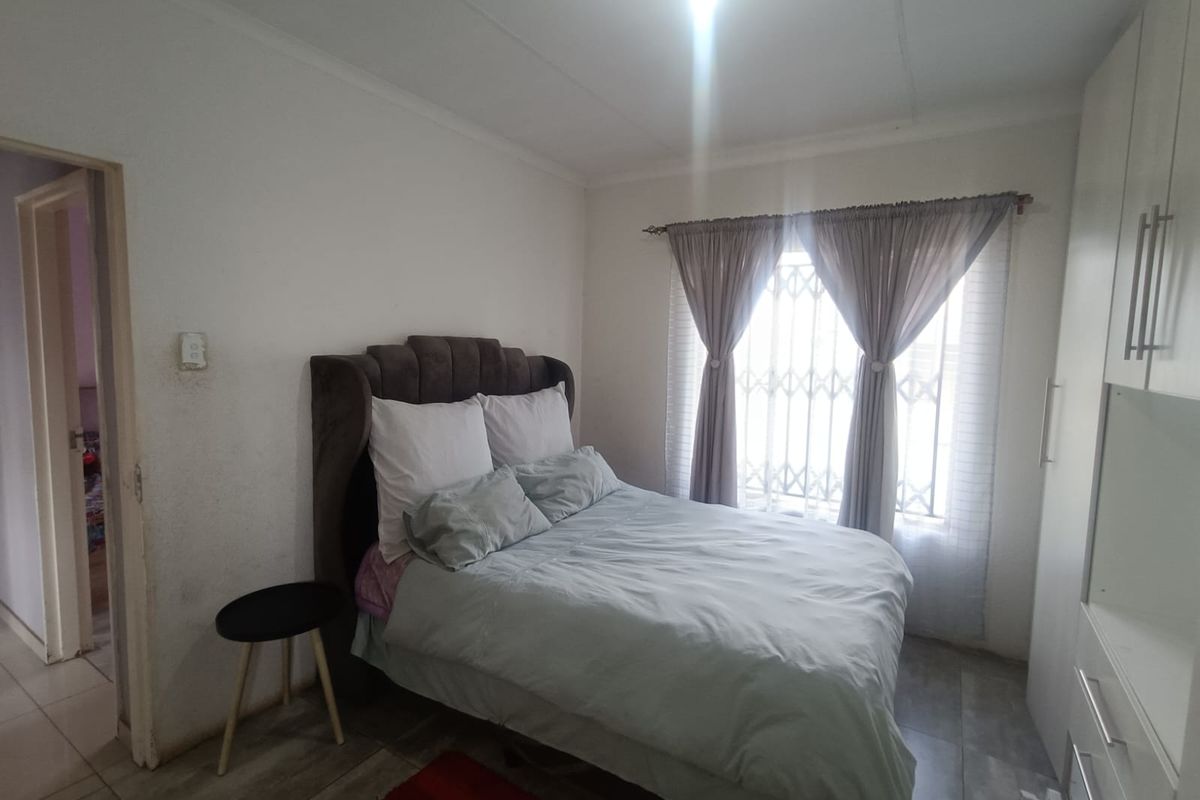 A functional bedroom featuring built-in cupboards, tiled flooring, and a window fitted with a security gate.