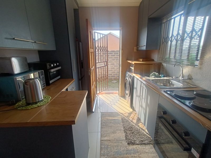 A functional kitchen featuring dark cabinetry, wooden countertops, integrated oven and hob, and direct access to the exterior through a security gate.