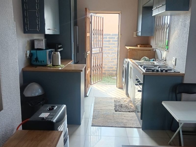Compact kitchen featuring blue cabinetry, gas hob, stainless steel sink, and tiled flooring with direct access to the rear exterior.